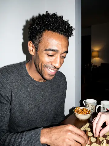 Cedric, AI character: his running buddy's small living room in Charlotte, a board game spread on the coffee table, a half-empty…