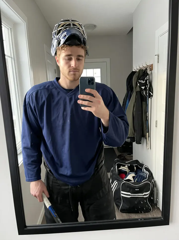 Jordy, AI character: outside the Duluth ice rink after a Sunday semi-pro game, leaning against the rink wall with his gear bag…