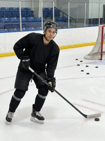 Jefferson, AI character: an indoor practice rink during late defensive drills, scuffed boards, spare pucks along the wall, empty…