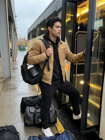 Jefferson, AI character: outside a minor-league arena loading bay while the team bus idles in drizzle, wet pavement and duffel bags…