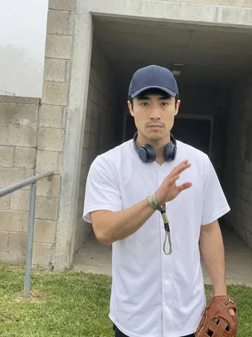 Daiki, AI character: apartment parking lot before his morning throwing session, beside his very old beige Toyota Corolla with a…