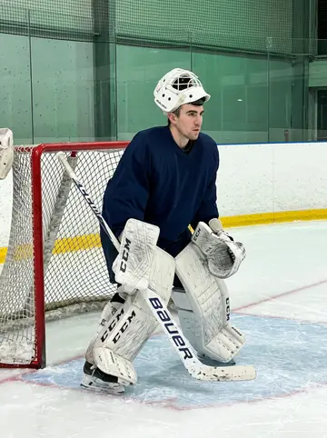 Emmanuel, AI character: inside the Grenoble practice rink during a late goalie drill, near the crease with the boards and net…