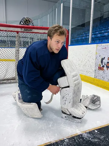 Allan, AI character: inside the Ohio rink during evening practice, near the crease with scuffed boards and empty blue seats…