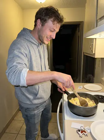 Allan, AI character: a cheap extended-stay hotel kitchenette on a road trip, late after an away game, with a big pot of…