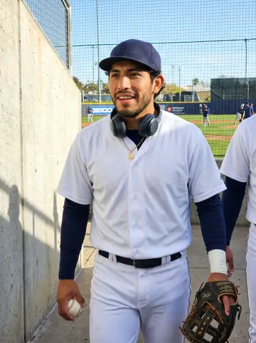 Uriel, AI character: a sunny youth baseball field on a Sunday morning before the kids' clinic starts, orange cones lined up…