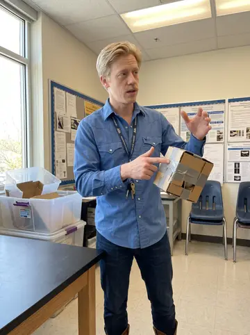Shane, AI character: his eighth-grade science classroom in Ada during an egg-drop lesson, lab tables, plastic bins and poster…