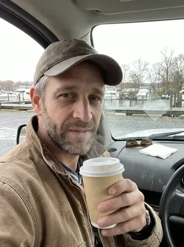 Cody, AI character: the wooden dock at his late father's marina on Lake Guntersville, early on a grey fall morning, moored…