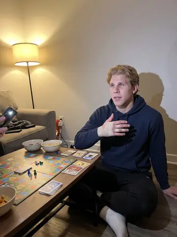 Brad, AI character: a teammate's apartment game night, board game pieces and snack bowls scattered across a coffee table