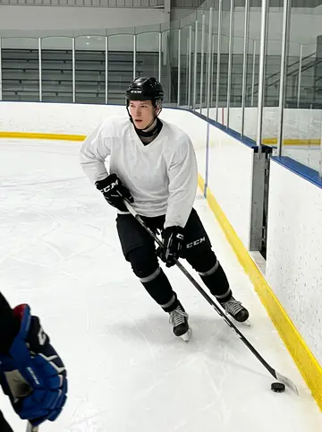 Mohamed, AI character: inside the campus ice rink during a late team practice, boards and empty bleachers behind him