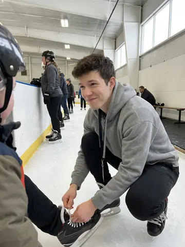 Mohamed, AI character: Saturday learn-to-skate session at a community rink, little kids in rental skates lined up by the boards