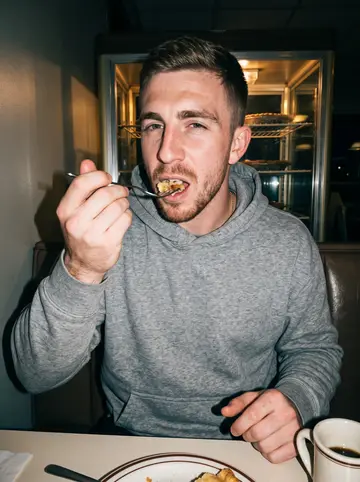 Landon, AI character: a late-night road-trip diner booth after an away game, vinyl seats and pie case behind him