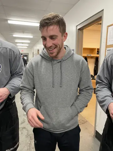 Landon, AI character: rink hallway outside the locker room after a home game, cropped teammates at both edges