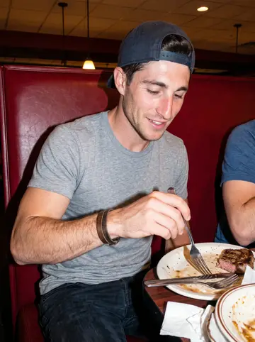 Finn, AI character: cheap Omaha steakhouse booth after a home game, red vinyl seat, half-empty plates and teammate elbows…