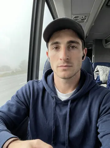 Finn, AI character: team bus leaving Omaha before sunrise, foggy highway visible through the window behind his seat