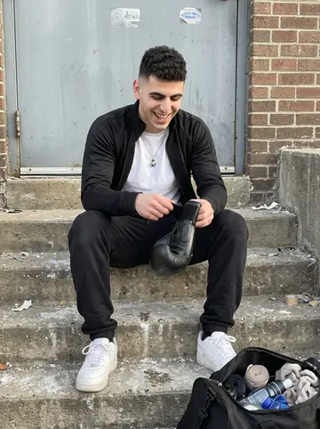 Benjamin, AI character: concrete steps behind the boxing gym after morning training, gym bag beside him