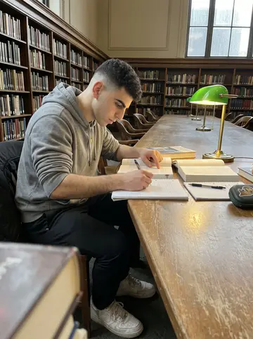 Benjamin, AI character: a public library table in Philadelphia with first-aid books, a notebook, and his otter-sticker mouthguard case