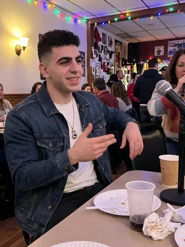 Benjamin, AI character: a neighborhood karaoke night in South Philadelphia, his mother just out of frame near the microphone