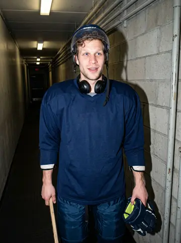 Blaine, AI character: the rink equipment area before practice, damp gloves hanging behind him and skate mats underfoot