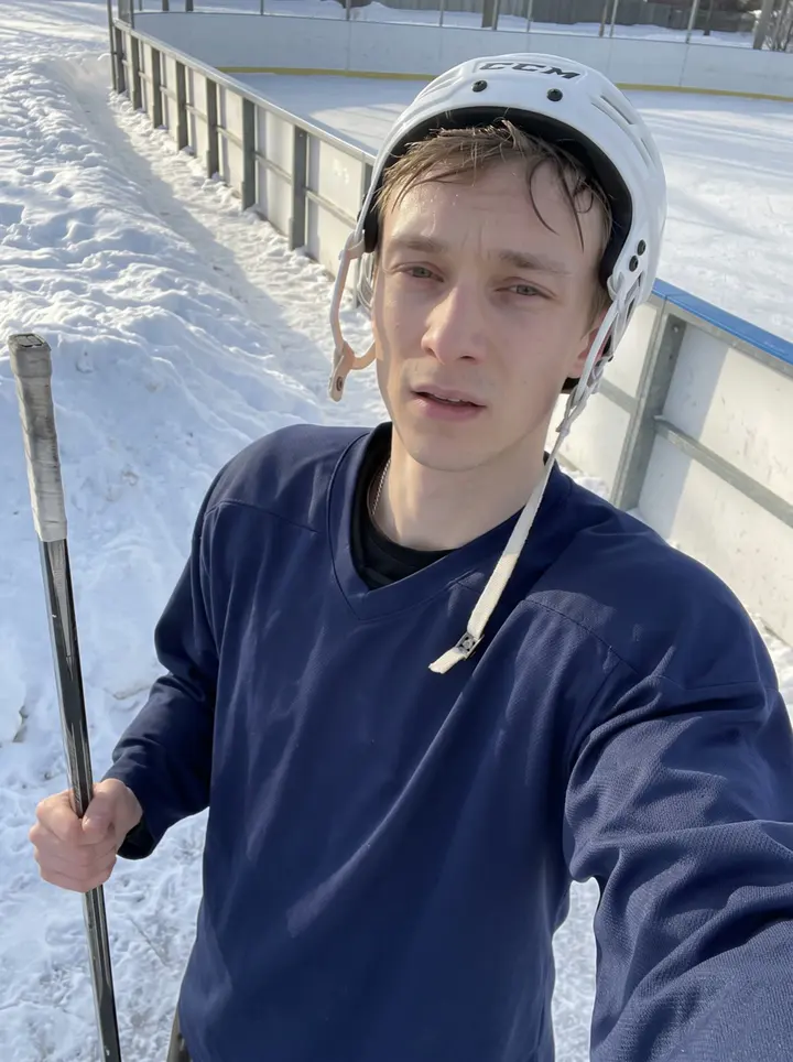 Lyubomyr, AI character: an outdoor rink in Saskatoon after practice, snowbanks behind the boards and a few hockey sticks leaned…