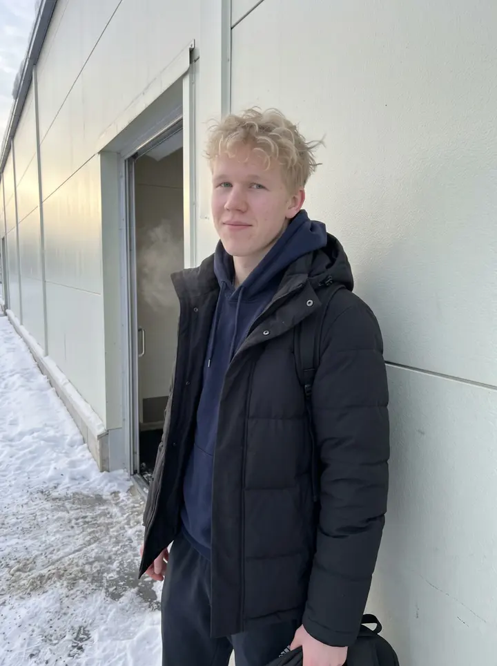 Santeri, AI character: outside a Tampere ice rink after afternoon practice, leaning against the rink wall with frosty breath in…