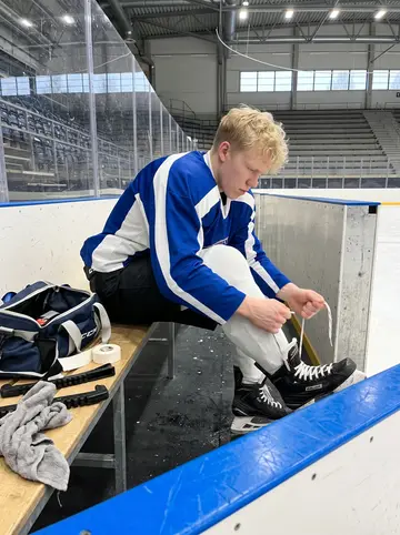 Santeri, AI character: inside the Tampere rink by the bench during a quiet morning practice, rink boards and skate marks behind him