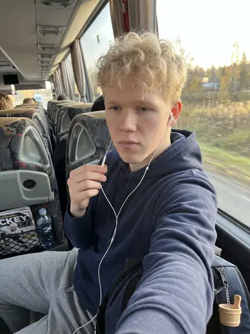 Santeri, AI character: team bus rolling out of Tampere toward an away game, fields and low sun visible through the window