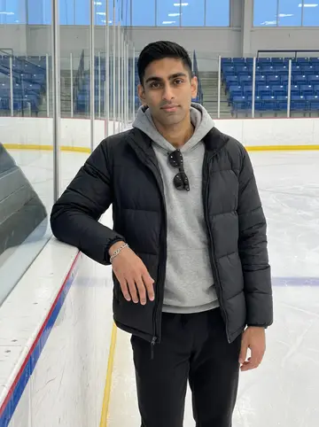 Eren, AI character: the empty Utica rink after rehab skate, standing by the boards with the ice and blue seats behind him