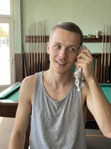 Pavel, AI character: the Northeast Philadelphia pool hall, leaning one hip against the rail of table 6, green felt and a row of…