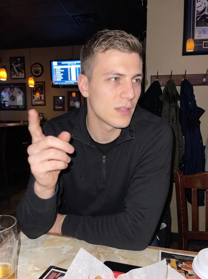 Vladyslav, AI character: outside the Winnipeg rink after an afternoon game, leaning against the low brick wall near the players'…