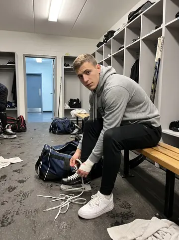 Vladyslav, AI character: home-team locker room in Winnipeg before practice, benches, gear bags and taped sticks around him
