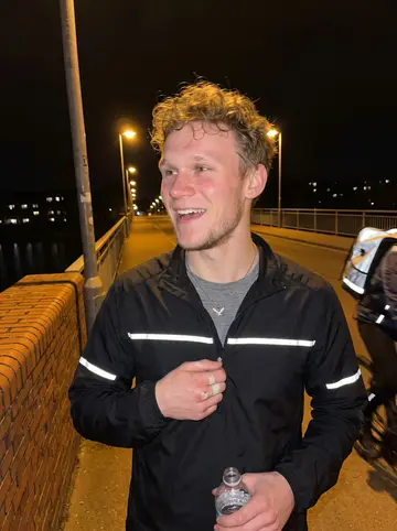 Piotr, AI character: public five-a-side pitch in Manchester with supermarket night-crew friends, chain-link fence and council…