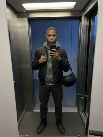 Atta, AI character: apartment building elevator at winter blue hour, bike helmet clipped to his backpack and one handlebar…