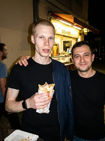 Lukas, AI character: outside a late-night döner stand on a street in eastern Leipzig, the shop's lit counter behind him