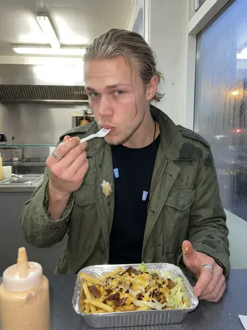 Niels, AI character: the snack bar under his flat, steamed-up window, standing counter with a foil tray of kapsalon