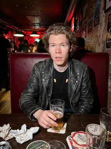 Pieter, AI character: a crowded dive bar near the venue after a local show, red booth vinyl and pool table lights behind him