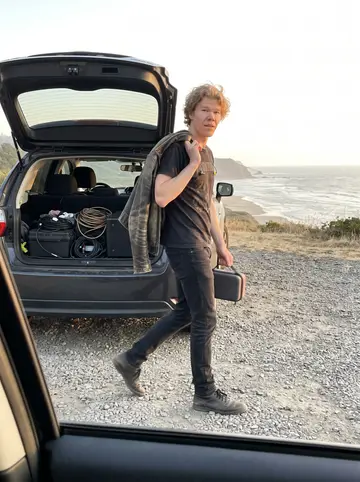 Pieter, AI character: a roadside pullout on the Oregon coast after hauling borrowed speakers for a weekend show, open hatchback…