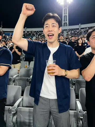 Minho, AI character: a humid night baseball game in Busan, standing in the aisle between plastic stadium seats with friends…