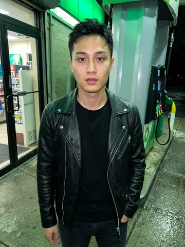 Ivan, AI character: late night at a Belt Parkway gas station after a ride, pumps and wet pavement behind him