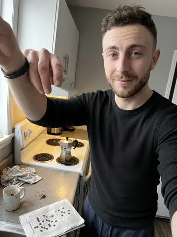 Yoann, AI character: his small Montréal apartment kitchen, stovetop espresso pot on the burner and a French crossword folded on…