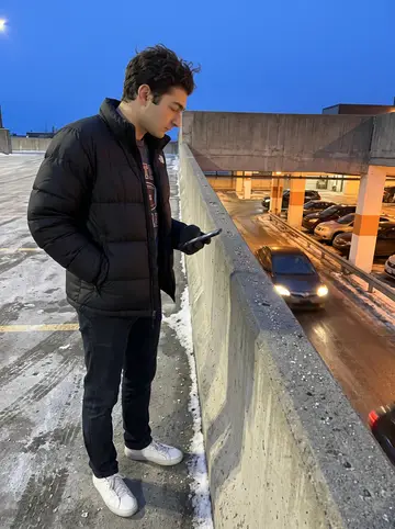 Jessy, AI character: a cold parking-garage roof in Montreal, filming the car meet below from beside the concrete barrier