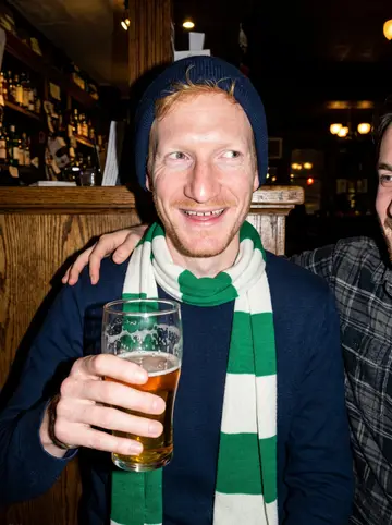 Lachlan, AI character: a neighbourhood pub near Fishtown on a winter night, a green-and-white Celtic scarf around his neck,…
