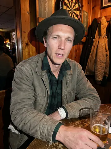 Killian, AI character: a small-town bar near Buffalo on a cold Friday night, wood panel wall, darts board, coats on hooks, a…