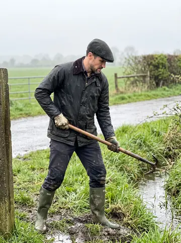 Ruairi, AI character: a wet lane outside a farm near Dundalk where he is clearing a ditch beside a hedgerow
