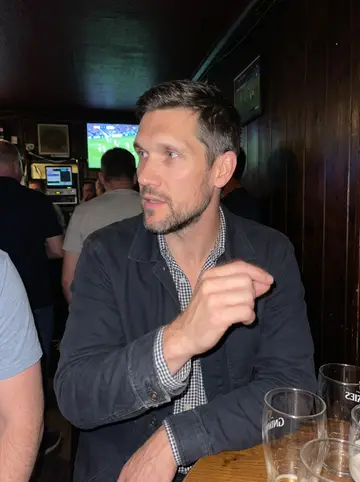 Ruairi, AI character: a crowded Dundalk pub during a hurling match on the radio, standing near a small table with empty pint glasses