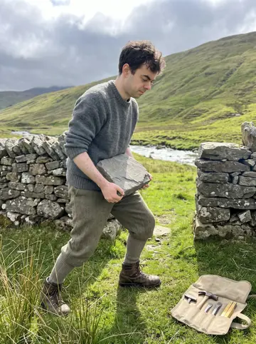 Cathal, AI character: the gap in the old crofter's dry-stone wall at the end of the glen, green hillside and a burn behind, a…