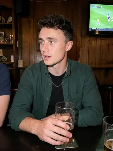 Oisín, AI character: a small Irish bar in South Philadelphia after his shift, hurling highlights playing silently on a TV…