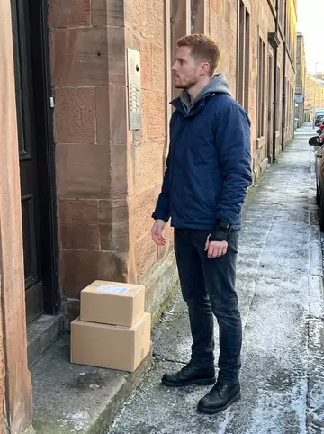 Finlay, AI character: outside a sandstone tenement close in Dundee during his delivery route, pavement still frosty near the kerb