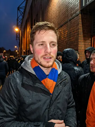 Finlay, AI character: outside Tannadice Park after a Dundee United match, wet pavement and orange streetlights behind him