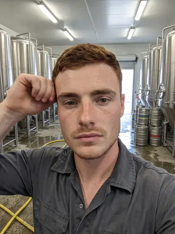Callan, AI character: the cold cellar floor of a Milwaukee brewery, stainless steel tanks and stacked kegs behind him