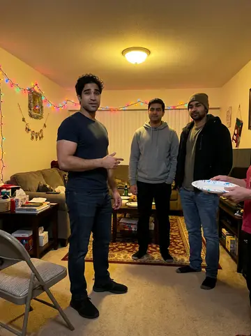 Graham, AI character: his aunt's living room at a family Christmas party, folding chairs pushed to the walls, colored string…